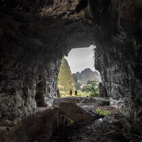 Two figures sillouetted in a cave opening