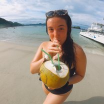 Standing on the beach on Isla Tortuga drinking a fresh coconut I picked, in front of our catamaran boat.