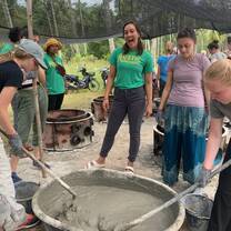 Program leader Marina smiling at the camera while the students mix cement to be poured into the fish house mold