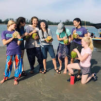 Some of the girls laughing and drinking from coconuts on a sandbar after planting mangrove seeds in a mudflat