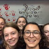 Team members are standing and smiling in front of a wall on which there is a painting of a turtle, made by hand-prints.