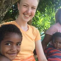 Zoe is sitting with Anna (small girl in the front), both are smiling. In the background Tutubai (small boy) looks unimpressed, while Ima laughs.