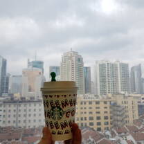 Holding a Starbucks cup in front of a window on the high floor of a building, overlooking Huangpu