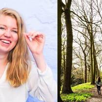 There is a smiling young woman moving her hair behind her ear, standing in front of a bright blue painted wall. Beside her, there is a picture of two people walking on a footpath between very tall, green trees.