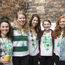 Five young women are smiling, wearing green beaded necklaces and face paint celebrating St. Patrick's Day.