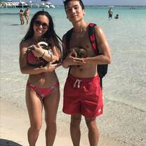 Two students are holding newborn puppies in front of the waterfront of the beach