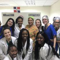 A group of students in their scrubs are smiling at the camera from in front of hospital cubicles