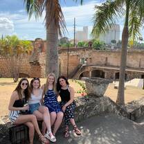 4 female participants are sitting on a concrete wall in front of a beach and palm trees