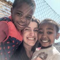 Voluntária abraçada com duas crianças sorridentes.