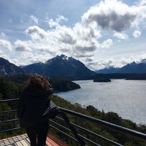 picture of girl with back facing camera in front of mountain and lake scenery