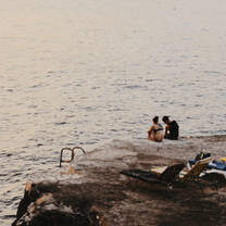 Two people sit by the sea