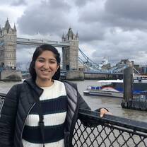 Student Gurjot Kang smiles in front of the tower bridge and thames river in London.