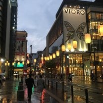 A city street in Japan on a rainy day with yellow lanterns hanging and lots of big shopping stores
