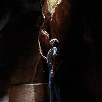 A girl standing in a cave looks up as light falls through a crack in the rock.