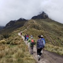 Students walk along green, grassy path towards mountain peak.