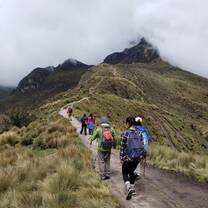 Students walk along green, grassy path towards mountain peak.