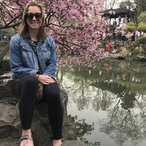 A young woman sitting on a rock with pink flowers behind her and a lake to the right