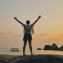 Standing, arms extended, facing the sunset over the beach in southern Goa.