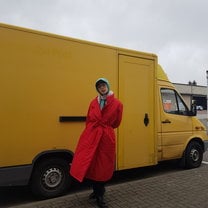 William is standing outside in bright winter clothes in front of a small, yellow truck.