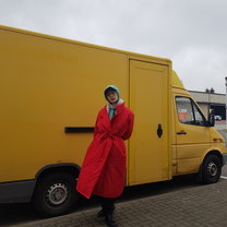 William is standing outside in bright winter clothes in front of a small, yellow truck.