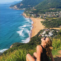 woman sitting on a bluff with a coastline behind her