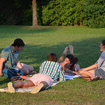Four talking and laughing students sitting in a circle on the campus lawn