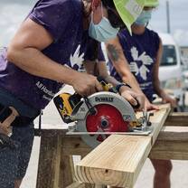 Volunteers use a circular saw to cut a two by four