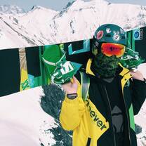 Snowboarder holding board in green and yellow jacket with helmet