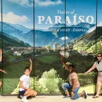 Four students posed in front of a backdrop photo of mountains and the text "Vuelve al Paradiso, vuelve a sentir Asturias"