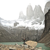 student throwing their arms up while standing on a rock with a vast mountain landscape behind them