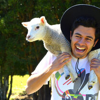 student wearing a large hat holding a baby sheep on his shoulders