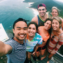 group of students taking a selfie on top of a tower with the Australian coastline behind and below them
