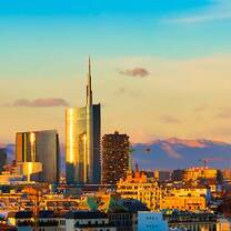 A cityscape -- urban buildings rise in the foreground with mountains in the background in evening light