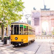 A yellow tram with a tall stone archway behind it