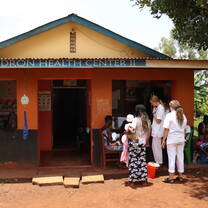 The front of the health center. Some patients and doctors are standing on the right side, it is time to give some vaccinations to the babies.