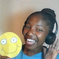 young female teacher holding up a big yellow happy face smiling wearing headphones