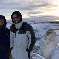 Two students in jackets stand in front of a snowy, rocky landscape