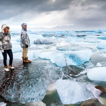 Two students, one male and one female, standing on a glacier, with a lake of glaciers behind them.