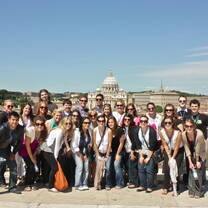 A large group of young people stand in front of the Vatican in Rome