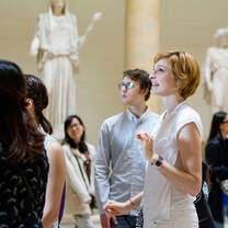 A professor explains a concept to students with statues in the background
