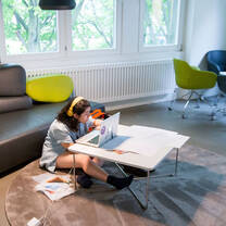 A student seated on the floor at a coffee table, working on their laptop