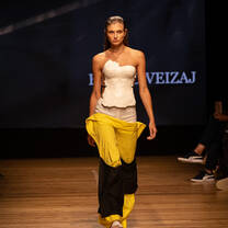 A model walking down the catwalk displaying fashion student creations with a white top and yellow and black trousers
