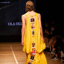 A model wearing a yellow garment with photographs down the back walking down the catwalk at an Accademia del Lusso Milan student fashion show