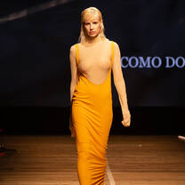 A model walking down the catwalk in an orange dress at the Accademia del Lusso student fashion show