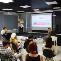 A group of student sit in a classroom, facing a projector screen