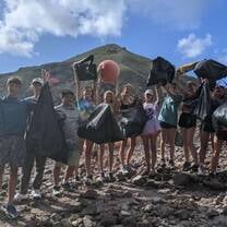 Group of teens on beach hold up bags of trash