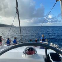 Helm of sailboat with group of teens sitting at the bow