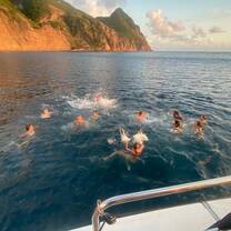 Group of teens swimming in ocean at sunset next to boat