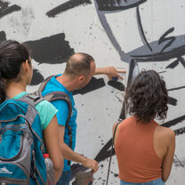 A man points to a graffiti on a wall in front of students
