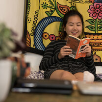 A student sits on a bed reading a book